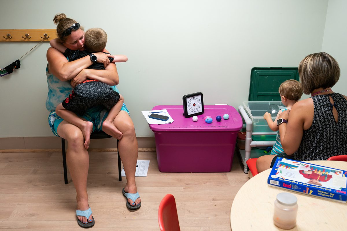 Augusta, ME, United States -- Lisa Hasch hugs her son Devon while Jay Patrick "J.P." works with Jessica L. Mosher, an OT assistant, during an occupational therapy session at All Kids in Action in Augusta, ME on Wednesday, August 8, 2018. Lisa Hasch adopted J.P. and his older brother Devon, and J.P. was an NAS baby who arrived at 4 weeks with withdrawal symptoms that included tremors, rashes, vomiting and constant screaming. J.P. got a feeding tub in July 2017 which improved his quality of life. (Photo by Yoon S. Byun)