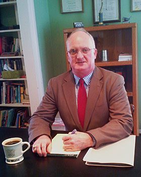 Christopher James Whalley sits at his desk as he prepares to write on a notepad