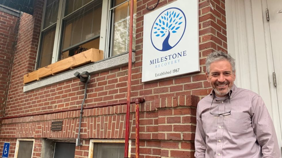 Tom Doherty, executive director of Milestone Recovery, smiles while standing underneath the organization's logo outside its offices