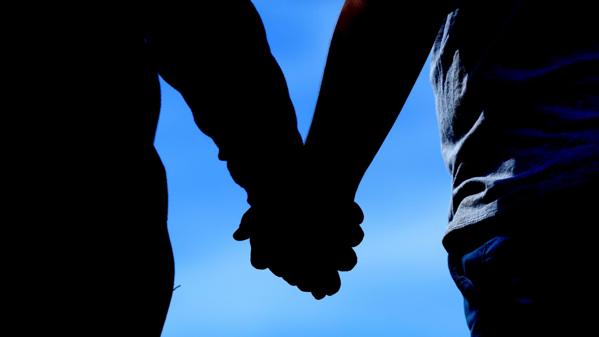 A silhouette image of two individuals holding hands