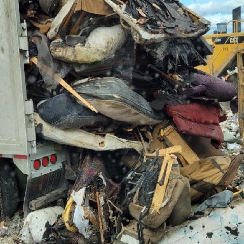 Trash such as cushions and textiles are poured from the back of a garbage truck into a landfill