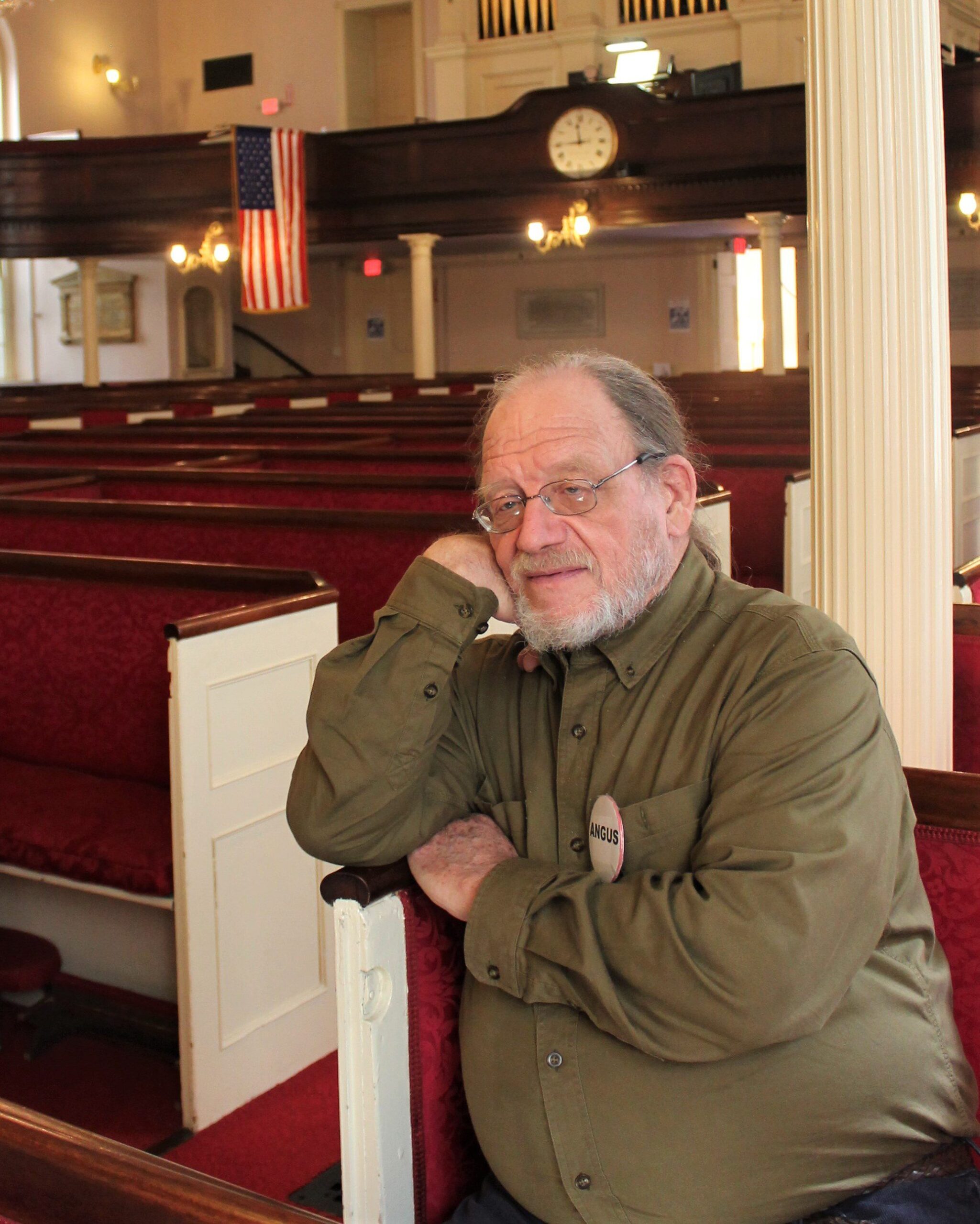 Angus Ferguson sits in one of many red church pews.