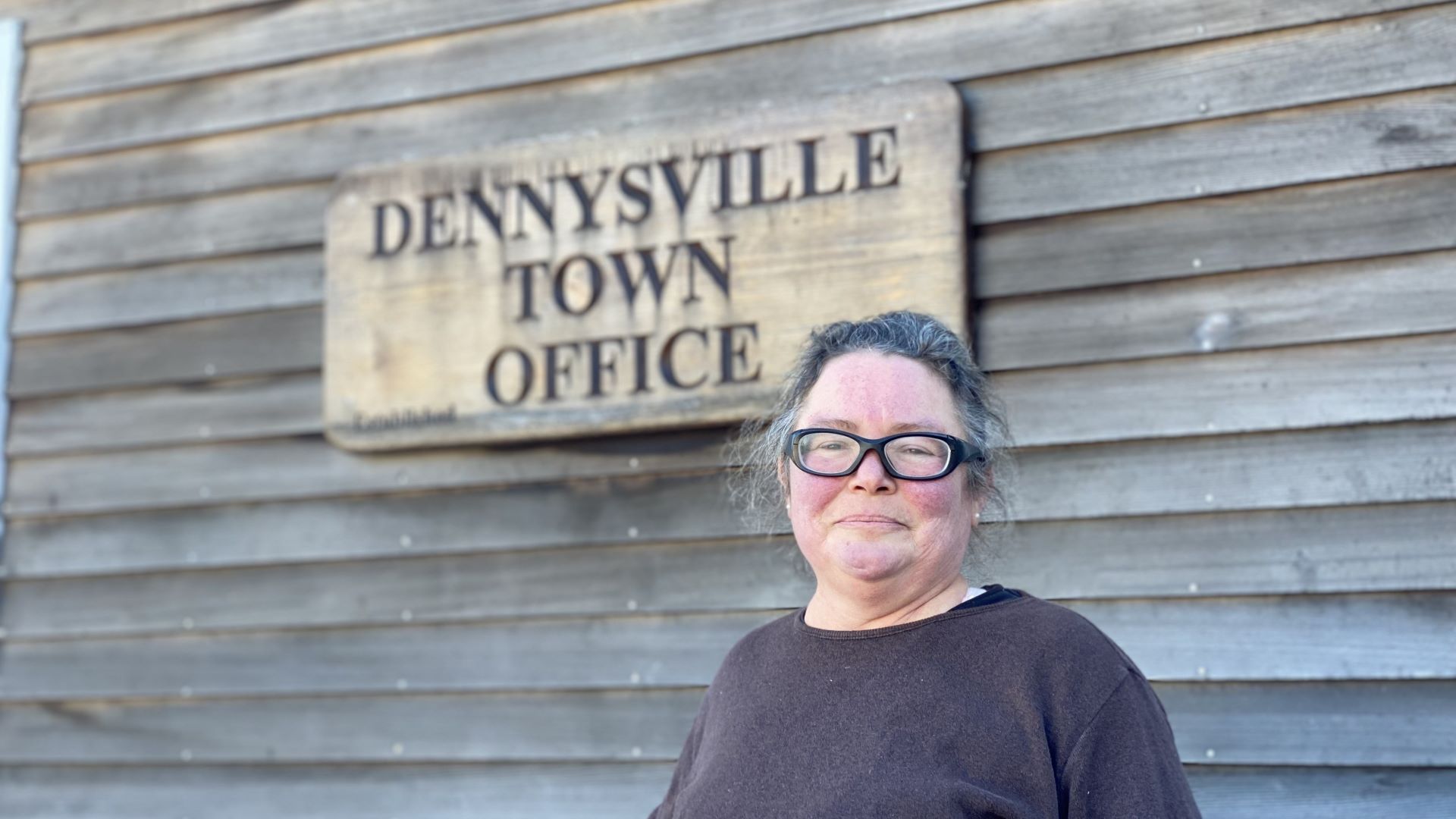 Violet Willis stands in front of a small sign attached to the exterior of the Dennysville town office.