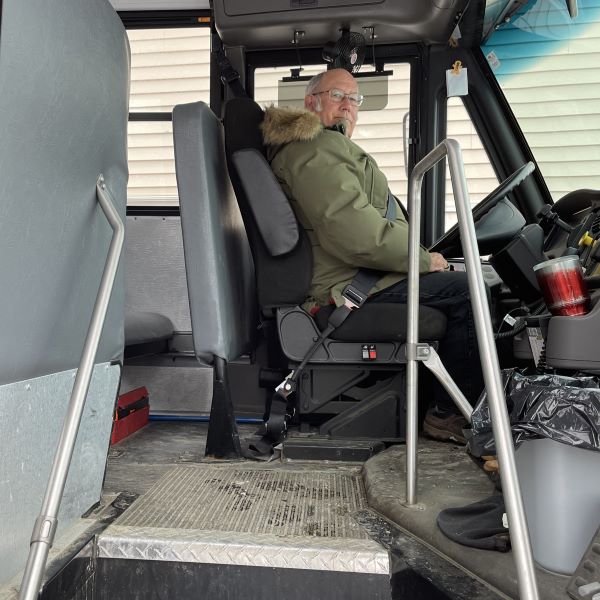 Mike Hinerman poses for a photo while sitting in the driver's seat of a school bus.